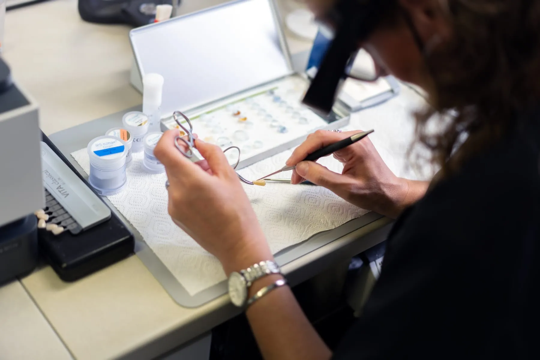 Feinarbeit an einer Keramikkrone, daneben Keramikmassen und ein Farbring